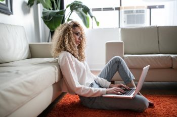 A woman sitting on the floor, using a laptop.